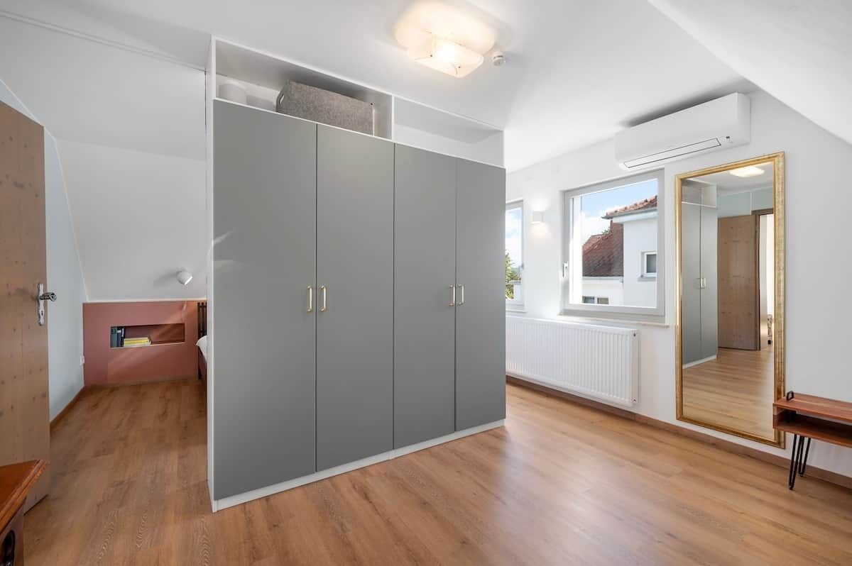 Et værelse med en grå garderobe, en træbænk, et spejl og en radiator.
