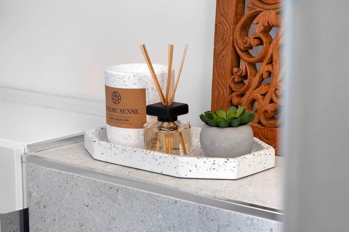 Una encimera de baño con un difusor, una vela y una planta pequeña.