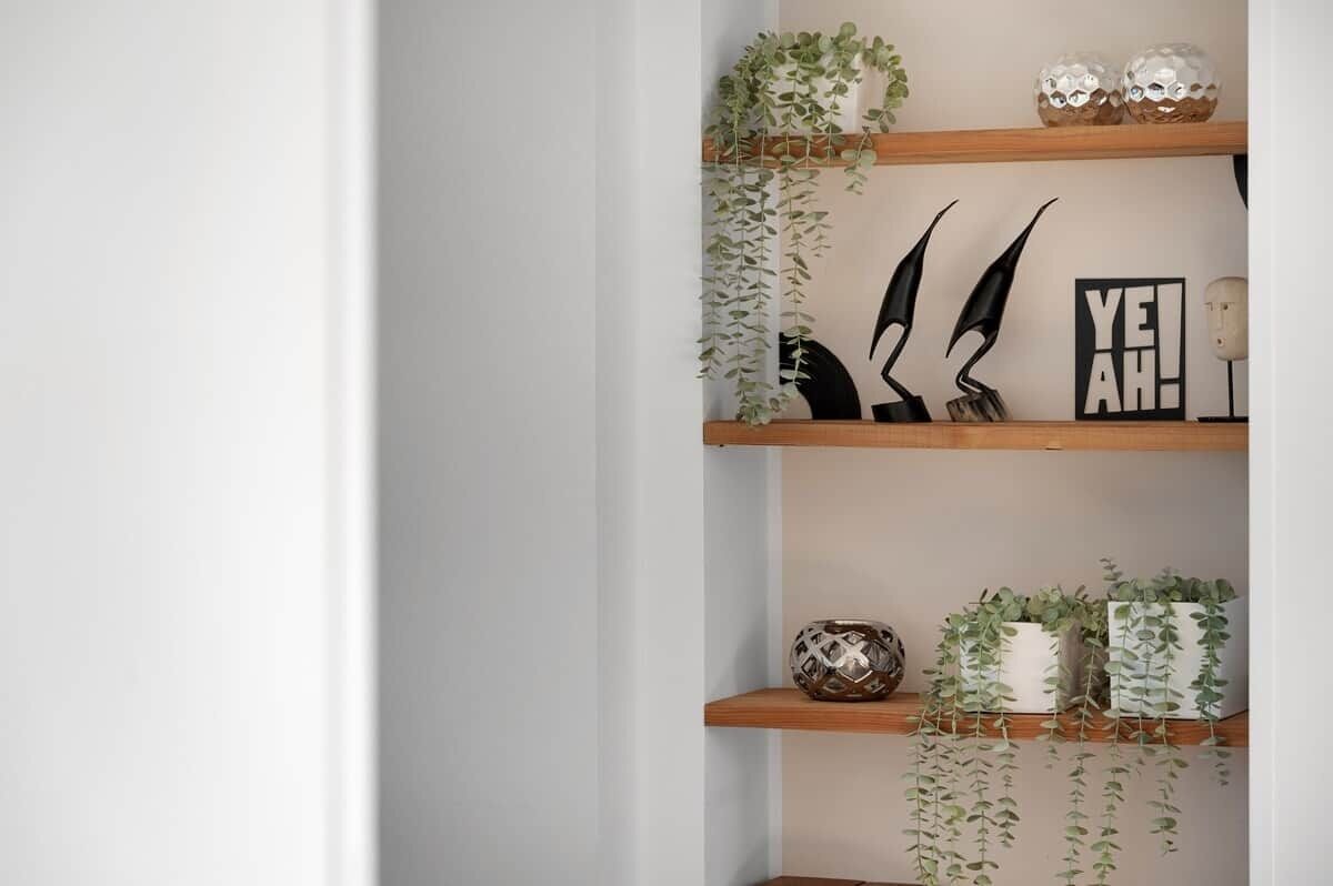 Uno scaffale con oggetti decorativi, tra cui una pianta, una scultura astratta in bianco e nero e un cartello con la scritta 'YE!AH!'.