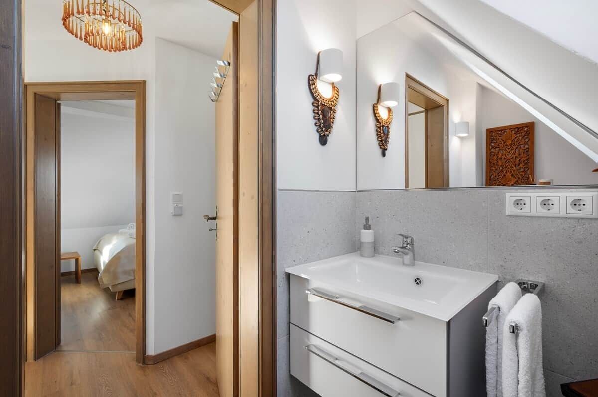 A modern bathroom with a large mirror, wall-mounted lights, a white sink, and a towel rack.