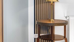 Een hoekzaak met een ronde houten tafel, een gouden lamp, een hangplant en een bevestigde televisie.