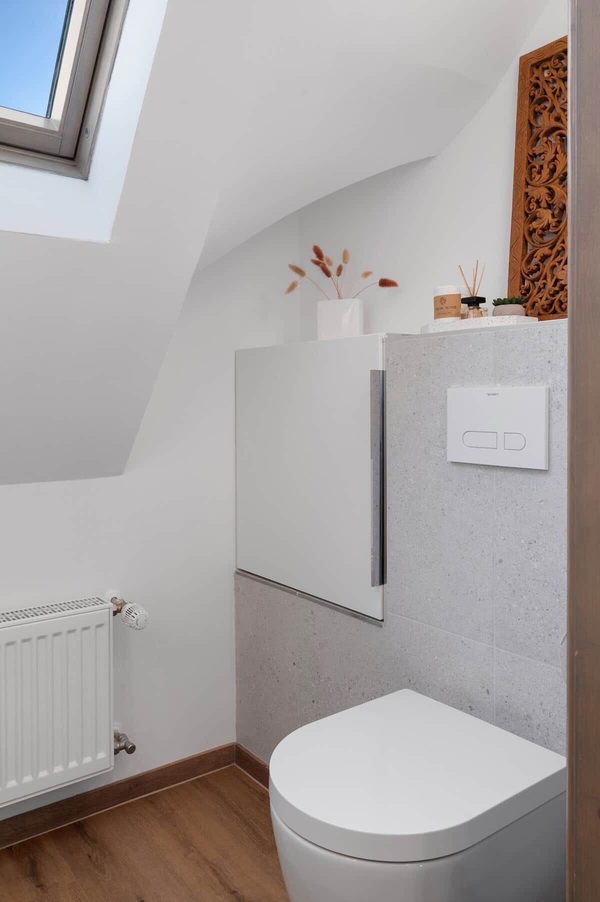 Un baño moderno con tragaluz, inodoro blanco, radiador y un adorno en la pared.