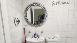 Ein Badezimmer mit weißem Waschbecken, Toilette und Spiegel mit dekorativem Rahmen.