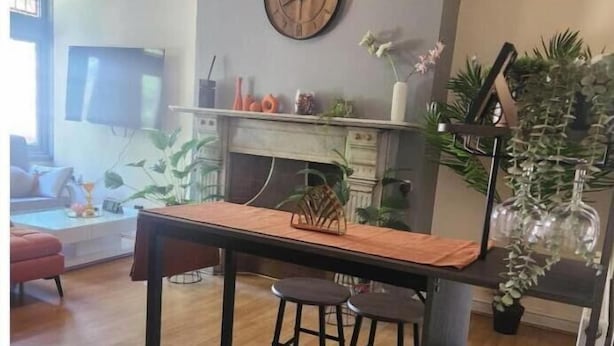 Ein Essbereich mit einem Holztisch, zwei Hocker, einer Wanduhr und einem Kamin.