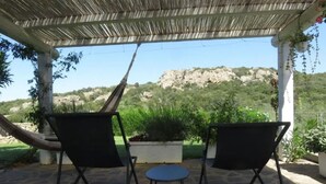 Un espacio de estar techado al aire libre con dos sillas y una mesita, con vistas a una ladera rocosa y cubierta de vegetación.