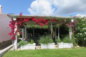 A covered patio with a pergola, white planters, and flowering plants. - The Pink House - Stunning view of the pool nestled in the greenery (San Pantaleo)