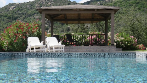 Una piscina con agua cristalina, un pabellón y sillas de descanso blancas.