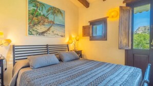 Un dormitorio con cama, un cuadro de una escena de playa, ventana con vistas y techo de madera.