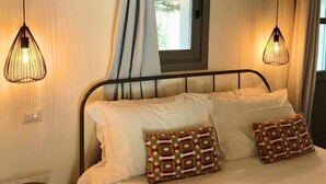 Un dormitorio con una cama, dos almohadas estampadas, una ventana con cortinas y dos lámparas colgantes.