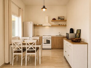 Eine kompakte Küche mit Essbereich, Holzschränken, einem weißen Kühlschrank und einer Pendelleuchte.