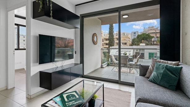 Un salon moderne doté d’un téléviseur à écran plat, d’un canapé, d’une table basse et d’un balcon offrant une vue sur la ville.