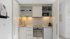 Une cuisine compacte avec des meubles blancs, un four encastré, un four à micro-ondes et une bouilloire.