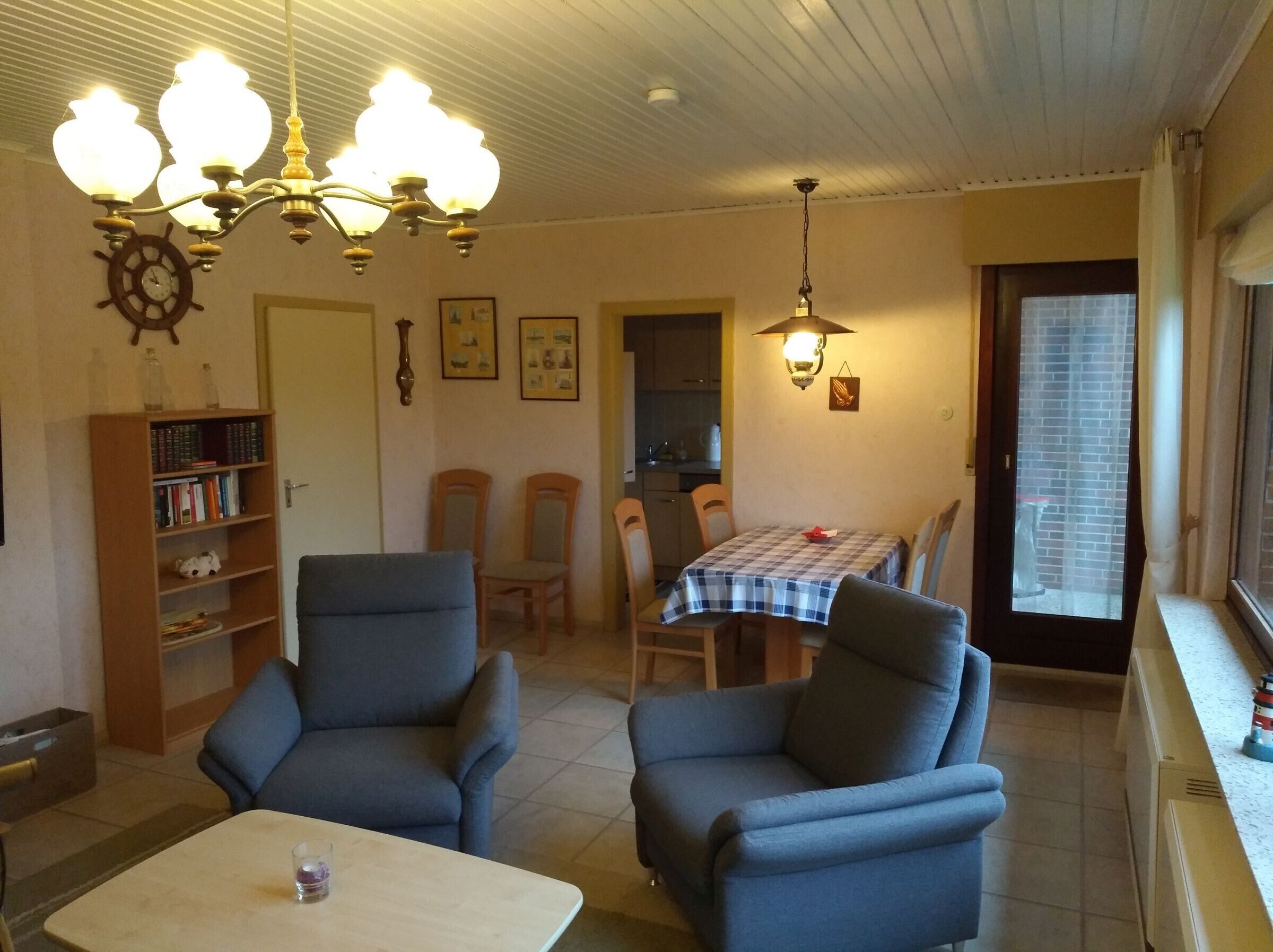 A living room with a dining area, a bookshelf, a clock, and a chandelier.