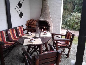 Um pátio com uma mesa redonda, cadeiras de madeira e um forno de tijolos.