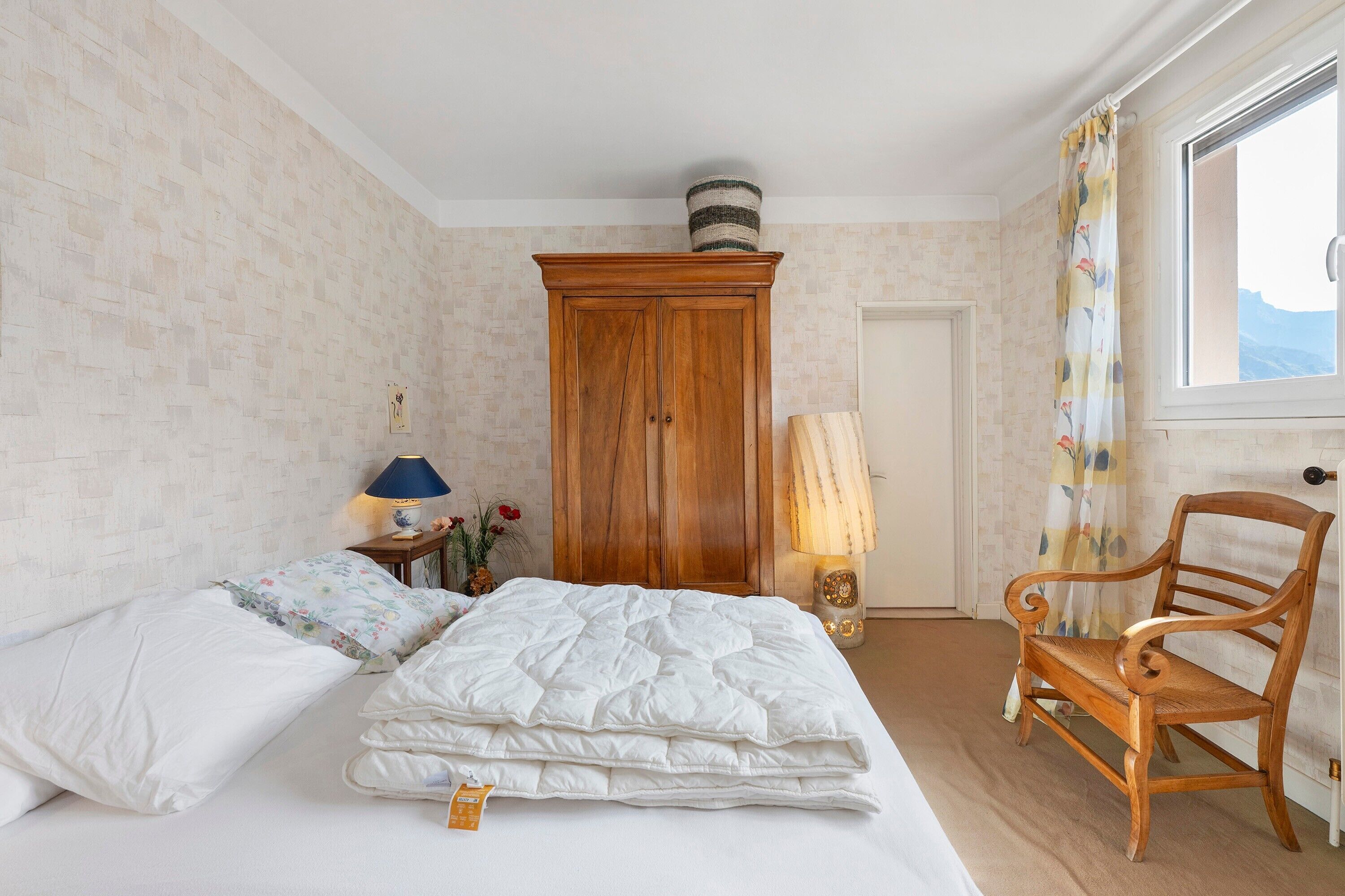 Une chambre à coucher avec un lit, une armoire en bois, une chaise, une lampe et une fenêtre donnant sur un beau paysage.