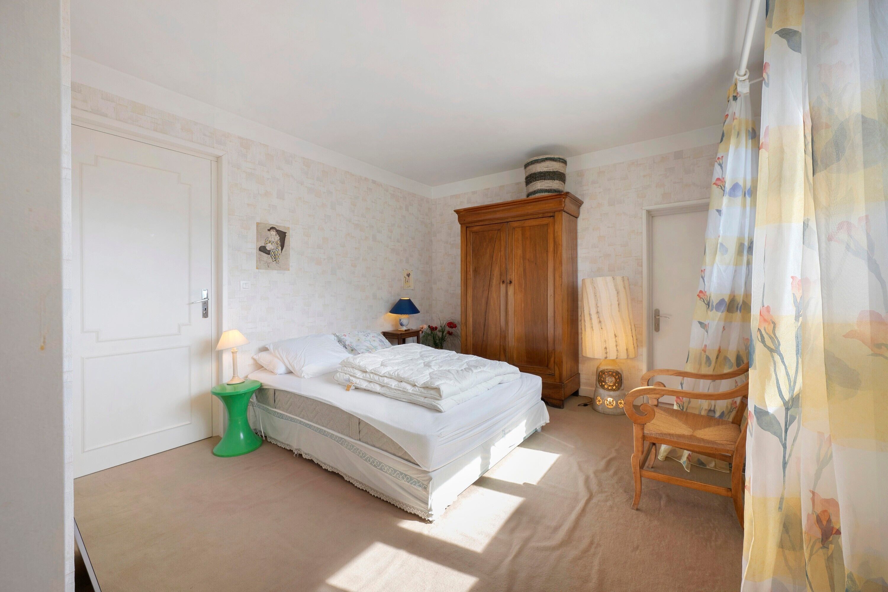 Un dormitorio con cama, un armario de madera, una silla, una lámpara y una cortina.