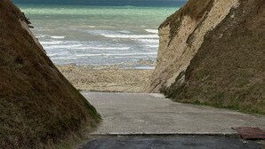 Une route côtière menant à une plage d’où l’on peut admirer l’océan et un ciel nuageux.