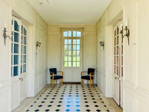 Un couloir avec un sol à carreaux, deux chaises et une porte à panneaux de verre.