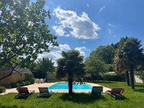 Una piscina con lettini, immersa nel verde e alberi.