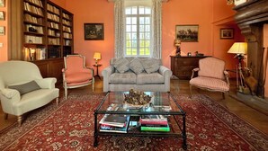 Un salon comprenant un canapé, des fauteuils, une table basse avec des livres, une cheminée et une bibliothèque.
