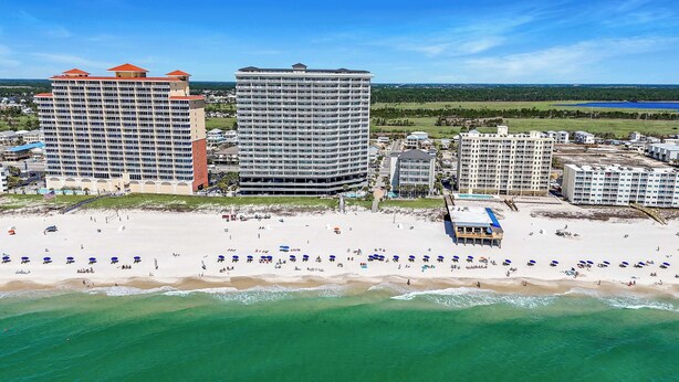 A beachfront hotel with multiple high-rise buildings, a sandy beach with umbrellas, and a clear view of the ocean. - Seawind 1602 Oceanfront (Gulf Shores)