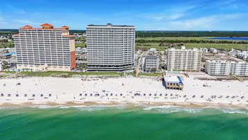 A beachfront hotel with multiple high-rise buildings, a sandy beach with umbrellas, and a clear view of the ocean.