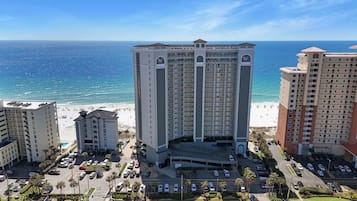 A high-rise hotel with multiple balconies, a parking lot, and a beach view.