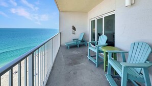 A balcony with a view of the ocean, two chairs, a table, and a wall-mounted light fixture. - Seawind 1602 Oceanfront (Gulf Shores)