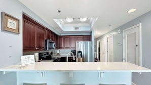A kitchen with wooden cabinets, stainless steel appliances, a central island with stools, and recessed ceiling lighting. - Seawind 1602 Oceanfront (Gulf Shores)