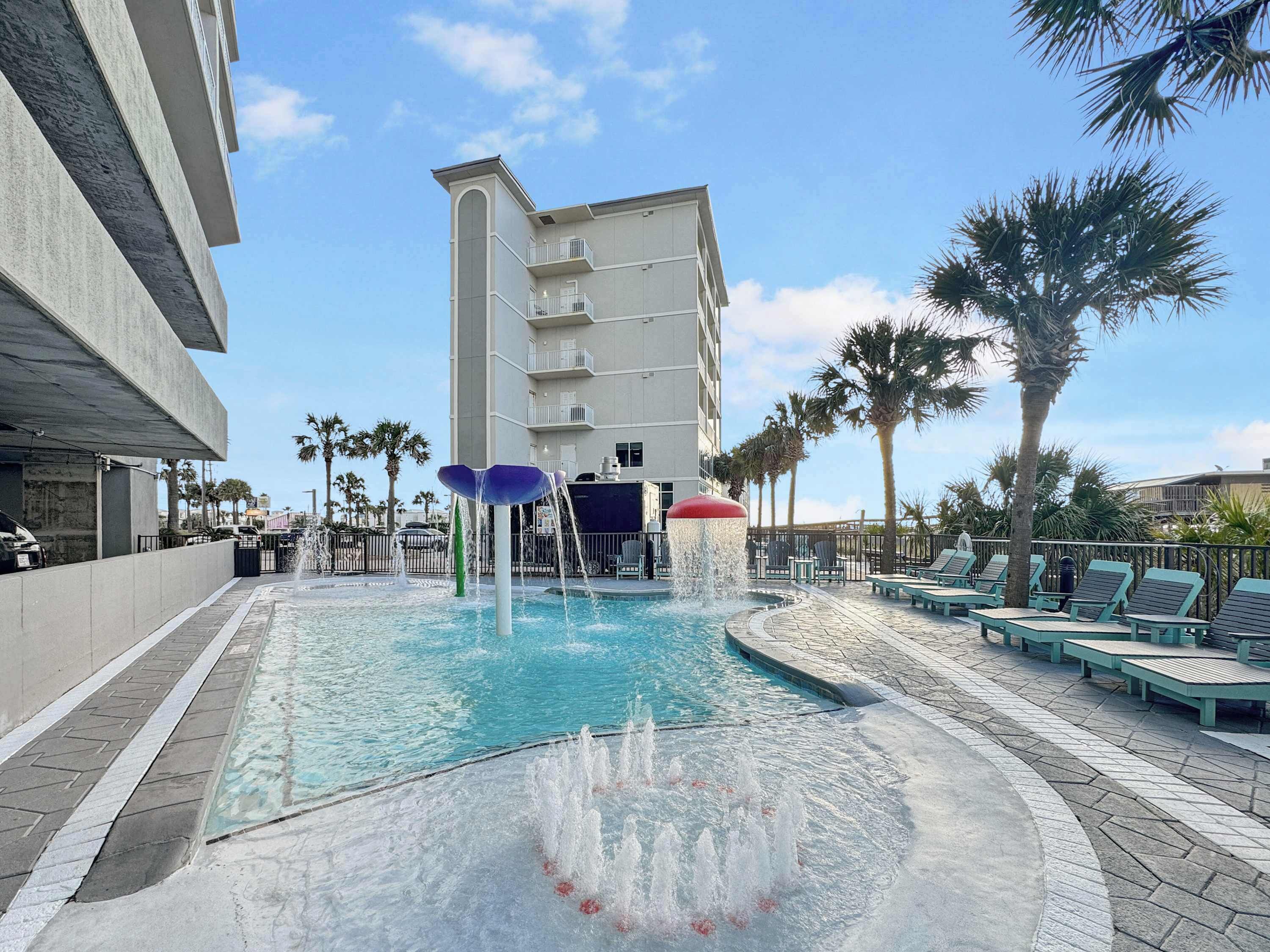 A swimming pool with water features, lounge chairs, and a building in the background.