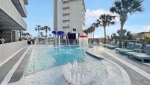 A swimming pool with water features, lounge chairs, and a building in the background. - Seawind 1602 Oceanfront (Gulf Shores)
