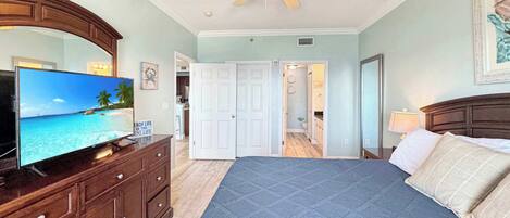 A bedroom with a bed, a television, a ceiling fan, a dresser, and a door leading to a bathroom.