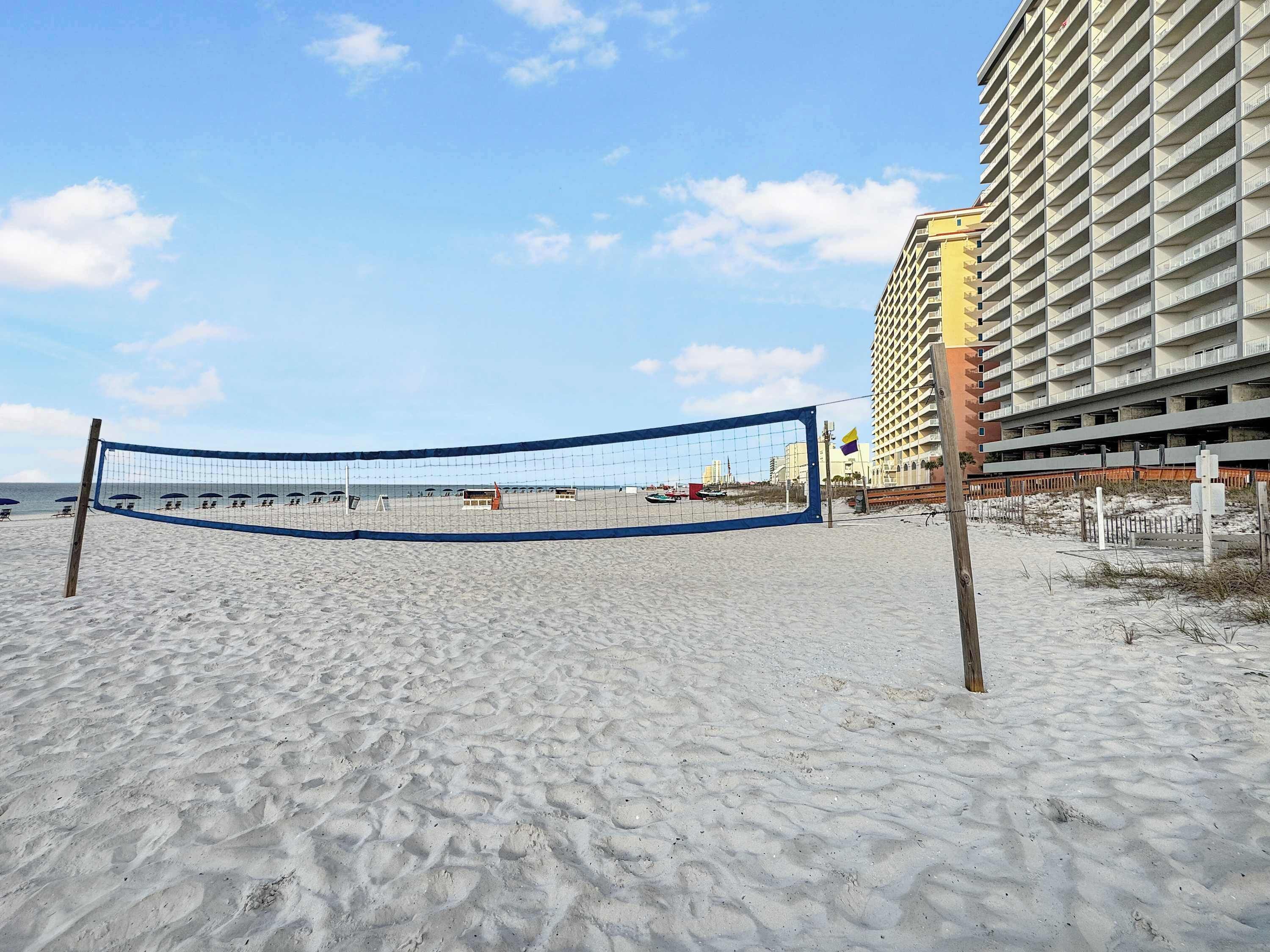 Una red de voleibol de playa sobre arena, con un rascacielos al fondo.