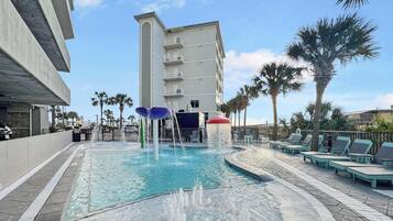 A swimming pool with water features, lounge chairs, and a building in the background.
