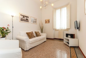 A living room with a white sofa, a floor lamp, a TV, and framed pictures on the wall. - Apartment just a few meters from the historic district of San Frediano in Florence! (Firenze)