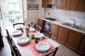 A dining area with a table set for four, a kitchen with wooden cabinets, a gas stove, and a sink. - Apartment just a few meters from the historic district of San Frediano in Florence! (Firenze)
