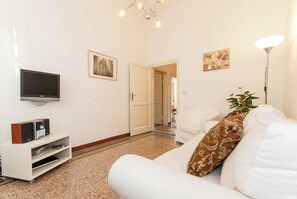 A living room with a flat-screen TV, a white sofa, a coffee table, a plant, and a painting on the wall. - Apartment just a few meters from the historic district of San Frediano in Florence! (Firenze)