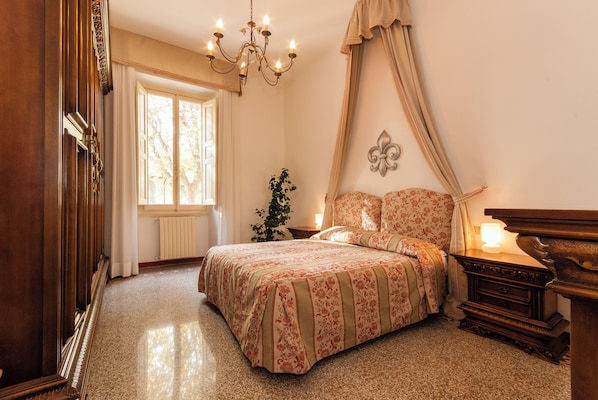 A bedroom with a large bed, a chandelier, a nightstand, and a window with curtains. - Apartment just a few meters from the historic district of San Frediano in Florence! (Firenze)