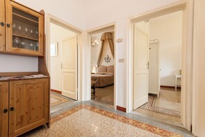 A hallway with a wooden cabinet, a patterned carpet, and a bedroom with a canopy bed. - Apartment just a few meters from the historic district of San Frediano in Florence! (Firenze)
