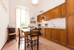 A kitchen with wooden cabinets, a dining table with chairs, a refrigerator, and a window with curtains. - Apartment just a few meters from the historic district of San Frediano in Florence! (Firenze)