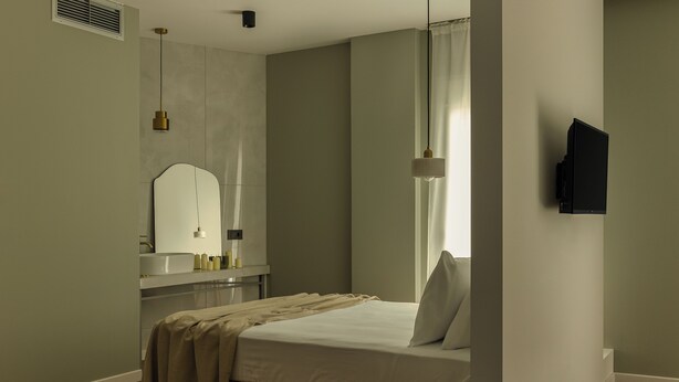 Een slaapkamer met een bed, nachtkastje, spiegel en een aan de muur bevestigde televisie.