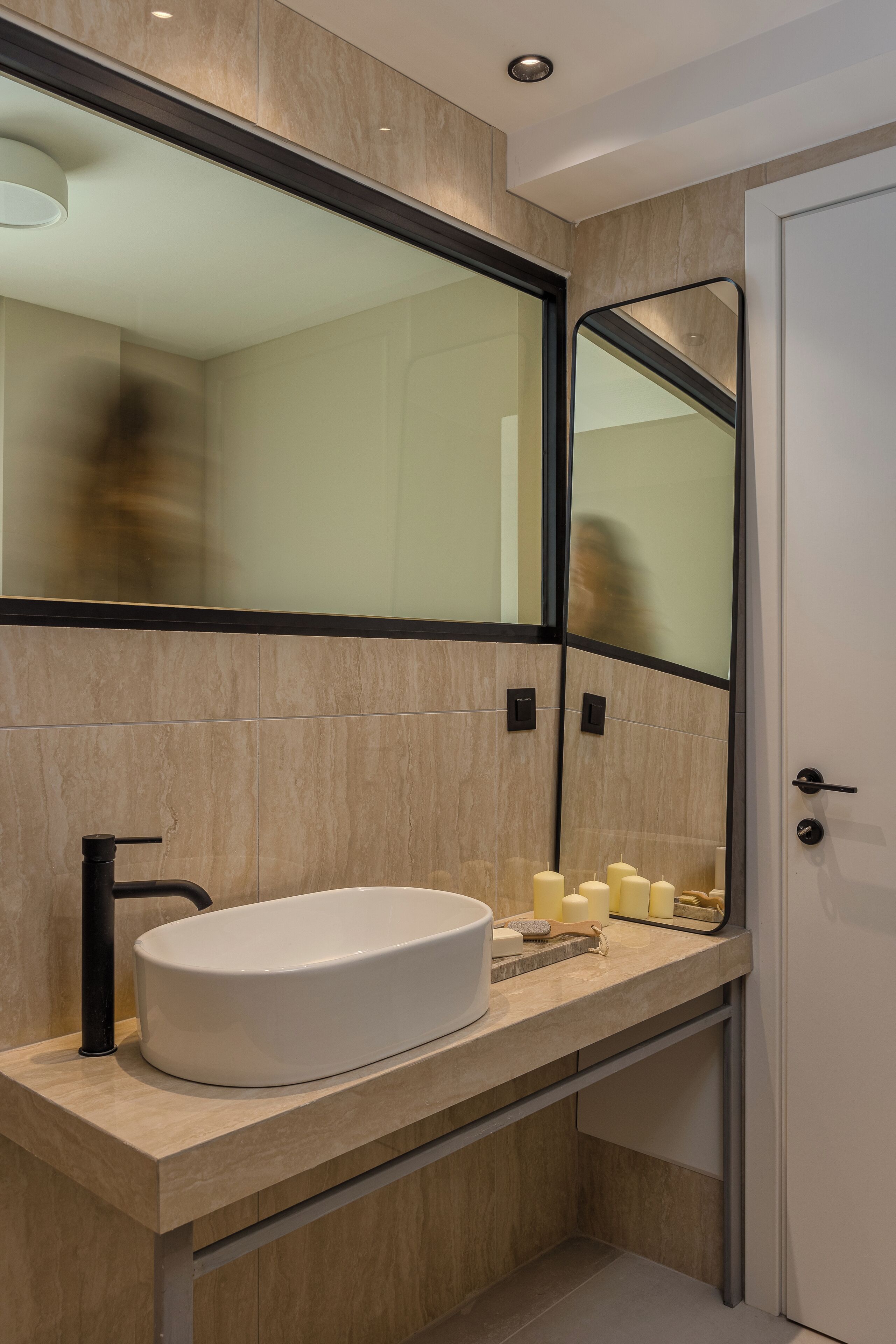 A modern bathroom with a large mirror, a white sink, and a door.