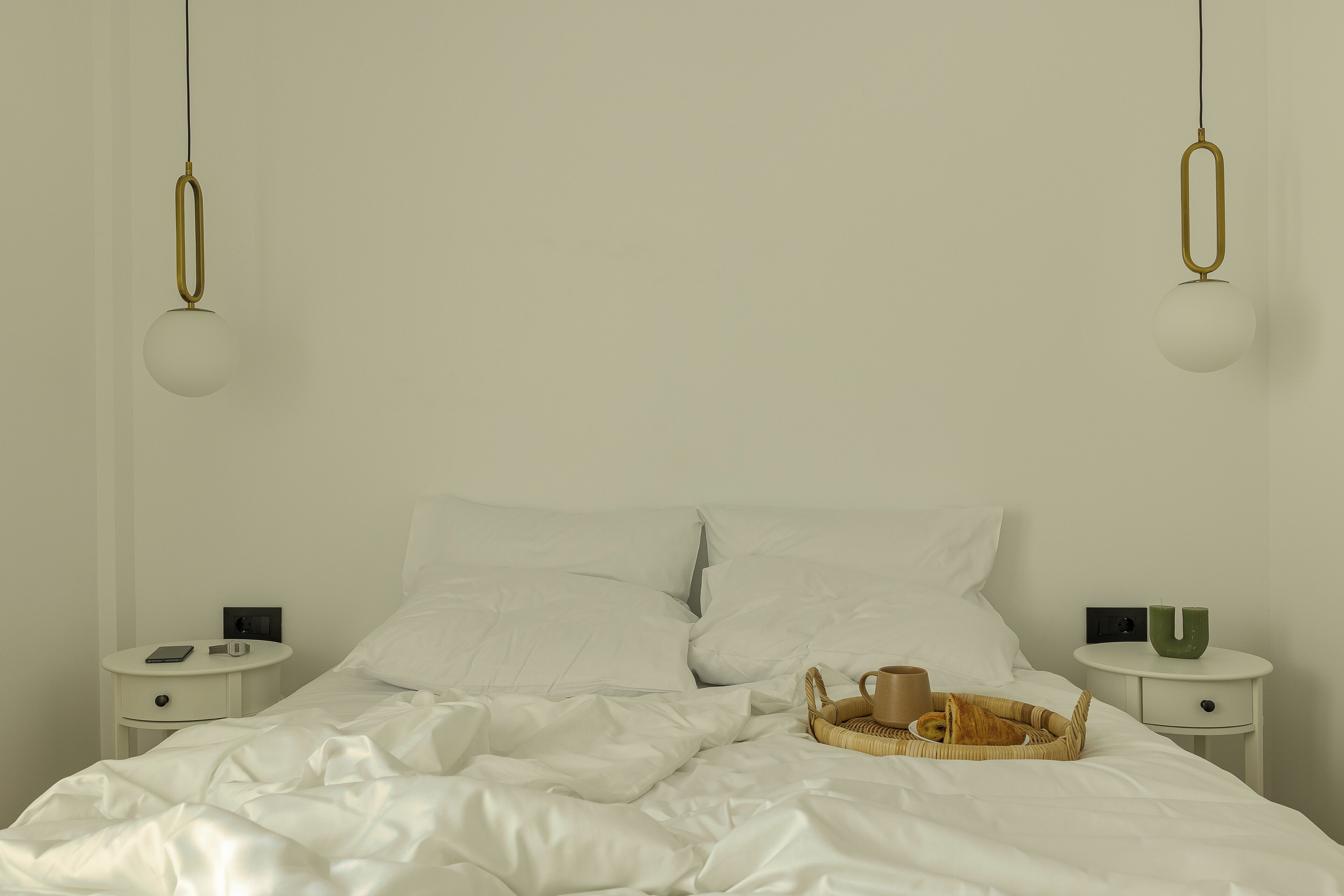 A neatly made bed with white linens, two bedside tables with lamps, and a basket with a mug on the right side.
