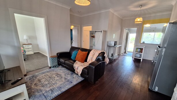 A spacious living area with a black leather sofa, a patterned rug, and a kitchen with a refrigerator and microwave. - South Bunbury Beach Shack (South Bunbury)