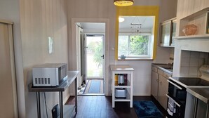 A compact kitchen with a microwave, toaster, and stove. A small table and a shelf with a kettle are also visible. - South Bunbury Beach Shack (South Bunbury)