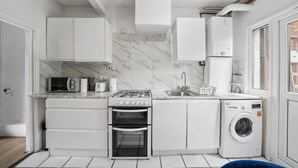 A compact kitchen with white cabinets, a built-in oven, a microwave, a sink, and a washing machine. - Cosy 2 Bed 5 Guests Garden Parking-wifi & Netflix (London)