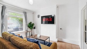 A living room with a sofa, a coffee table, a plant, and a wall-mounted TV displaying the Netflix logo. - Cosy 2 Bed 5 Guests Garden Parking-wifi & Netflix (London)