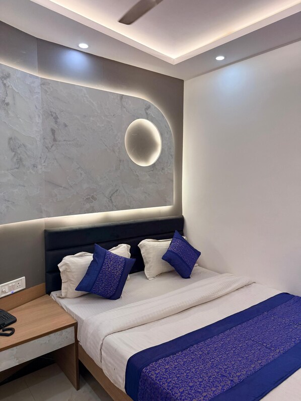 A modern bedroom with a bed, bedside table, and a wall-mounted light fixture. - Hotel Amba Deluxe (New Delhi)
