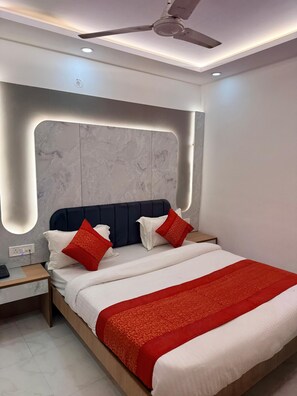 A modern bedroom with a bed, nightstand, and ceiling fan. - Hotel Amba Deluxe (New Delhi)