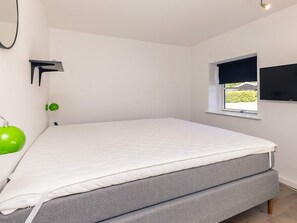 A bedroom with a bed, a window, a wall-mounted TV, and a green lamp. - 4 Star Holiday Home in Vaeggerlose (Vaeggerlose)